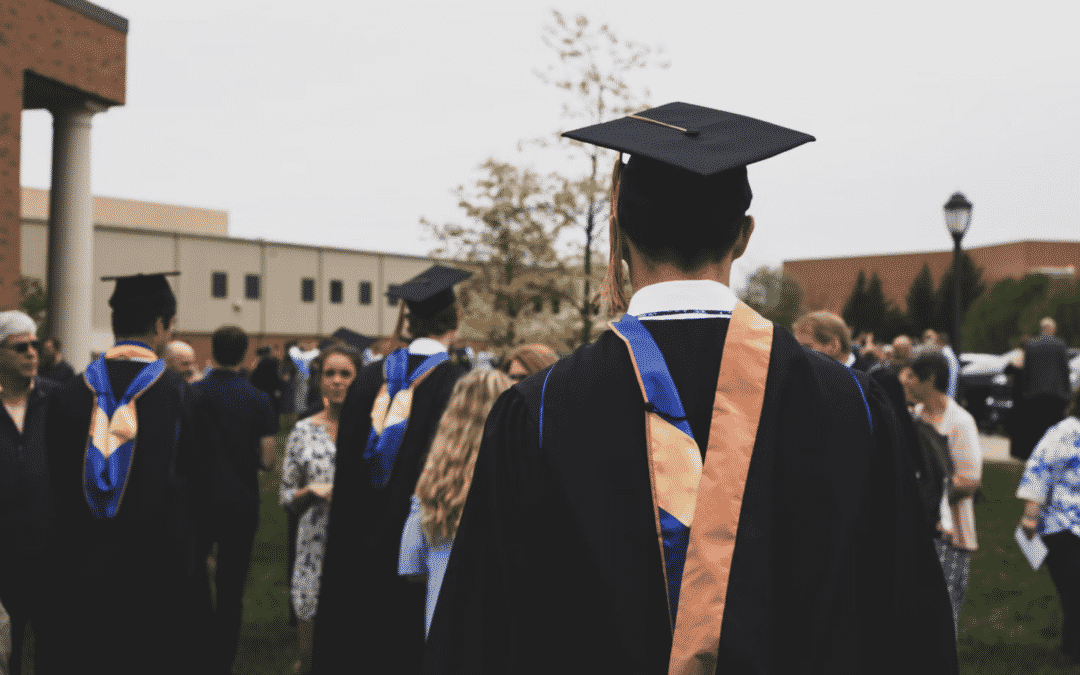 College graduate in cap and gown standing outside with other graduates